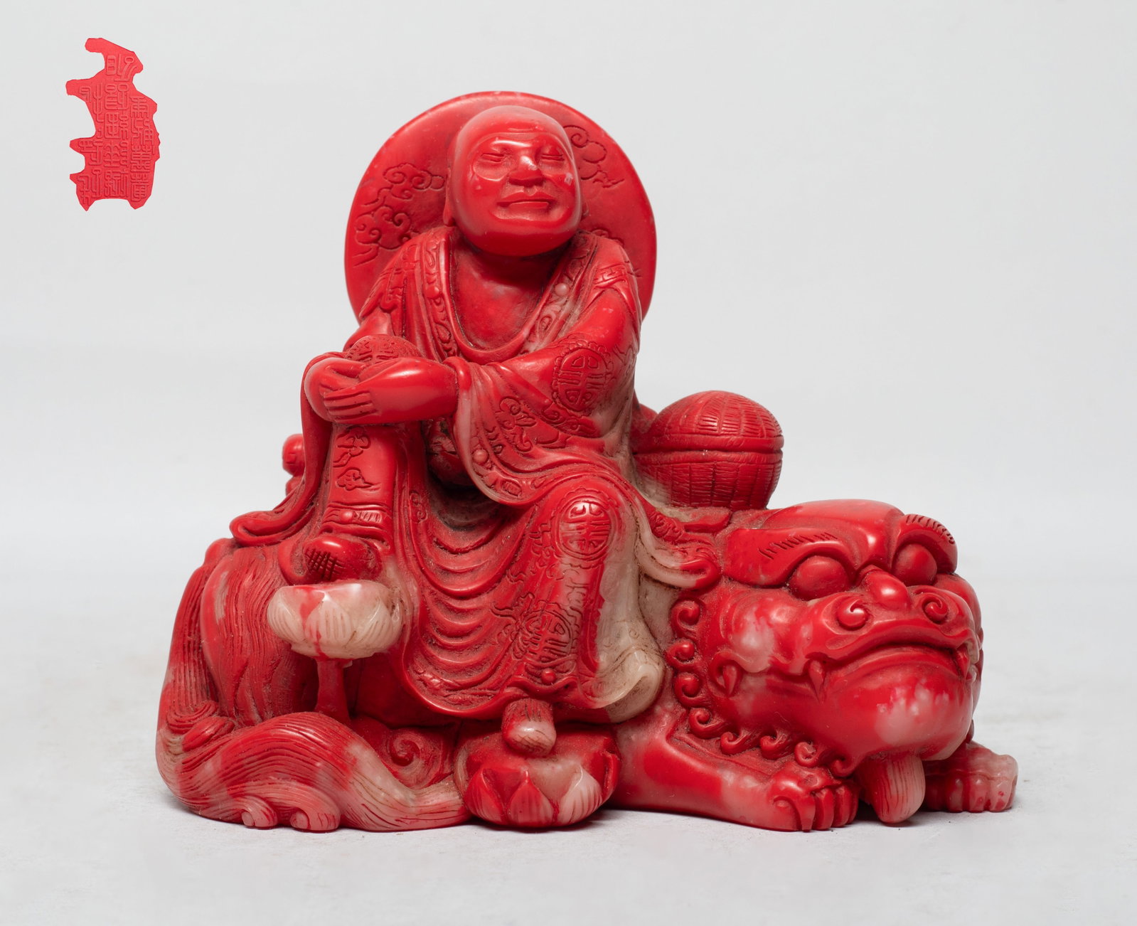 Chinese Export Stone Sculpture of Luohan: The Luohan carved seated on the recumbent beast, his feet stepping on lotus, wearing a long flowing robe inscribed with shou characters and clouds, the beast back supporting books and a box. Approx.