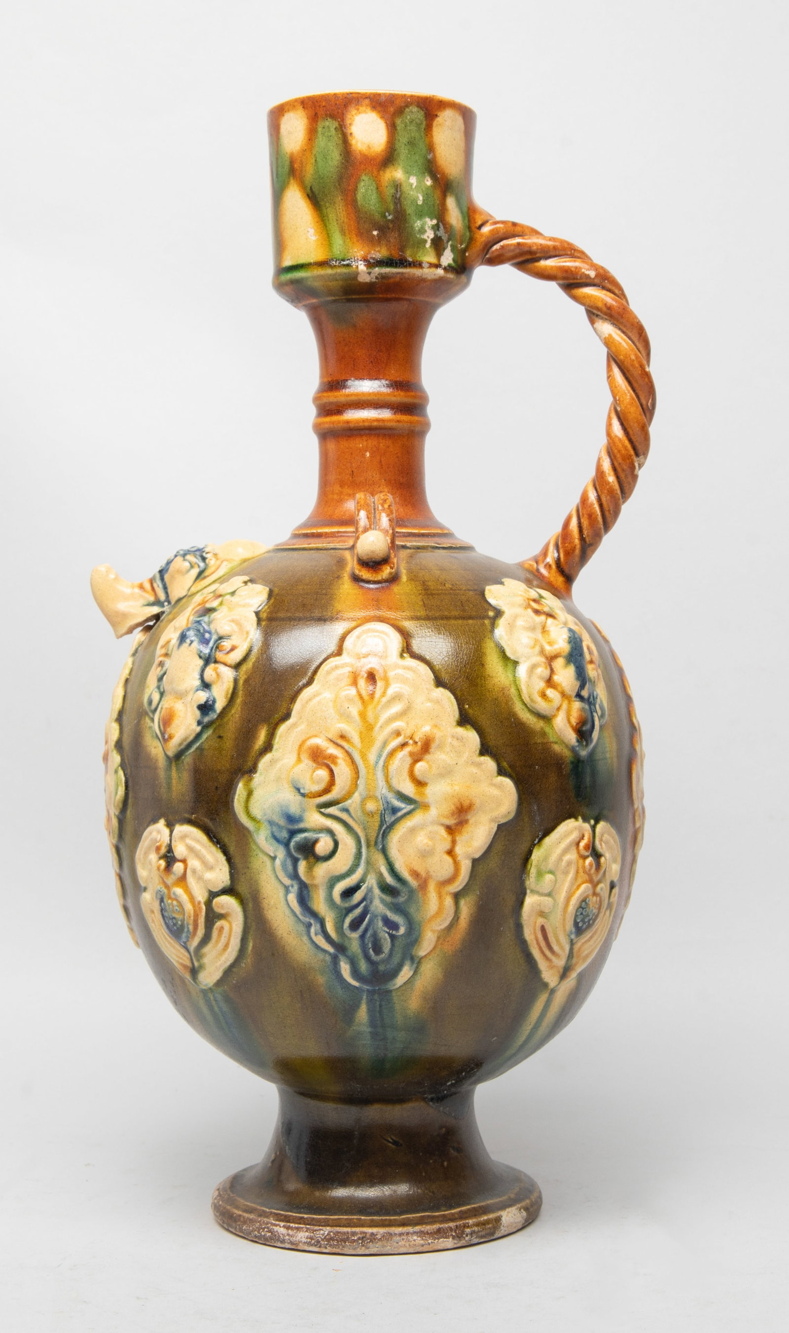 Tall Chinese Sanchai Porcelain Vase: The globular body carved in raised relief with stylized motif, rising from a spreading foot to columnar neck and mouth, with a twisted rope form handle, the exterior applied with creamy, brown, green