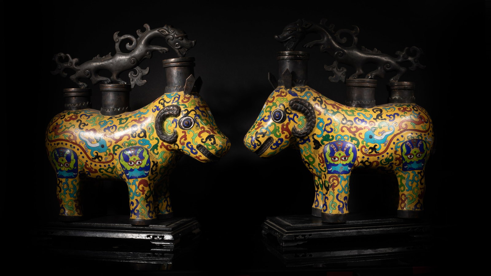 Pair Chinese Cloisonne Beast Vases W/Stand: Each in the form of the ram beast in standing position, featuring a bright yellow, red, and blue decorative with three cylindrical containers and a mythical beast perched on top, with fitted wood stan