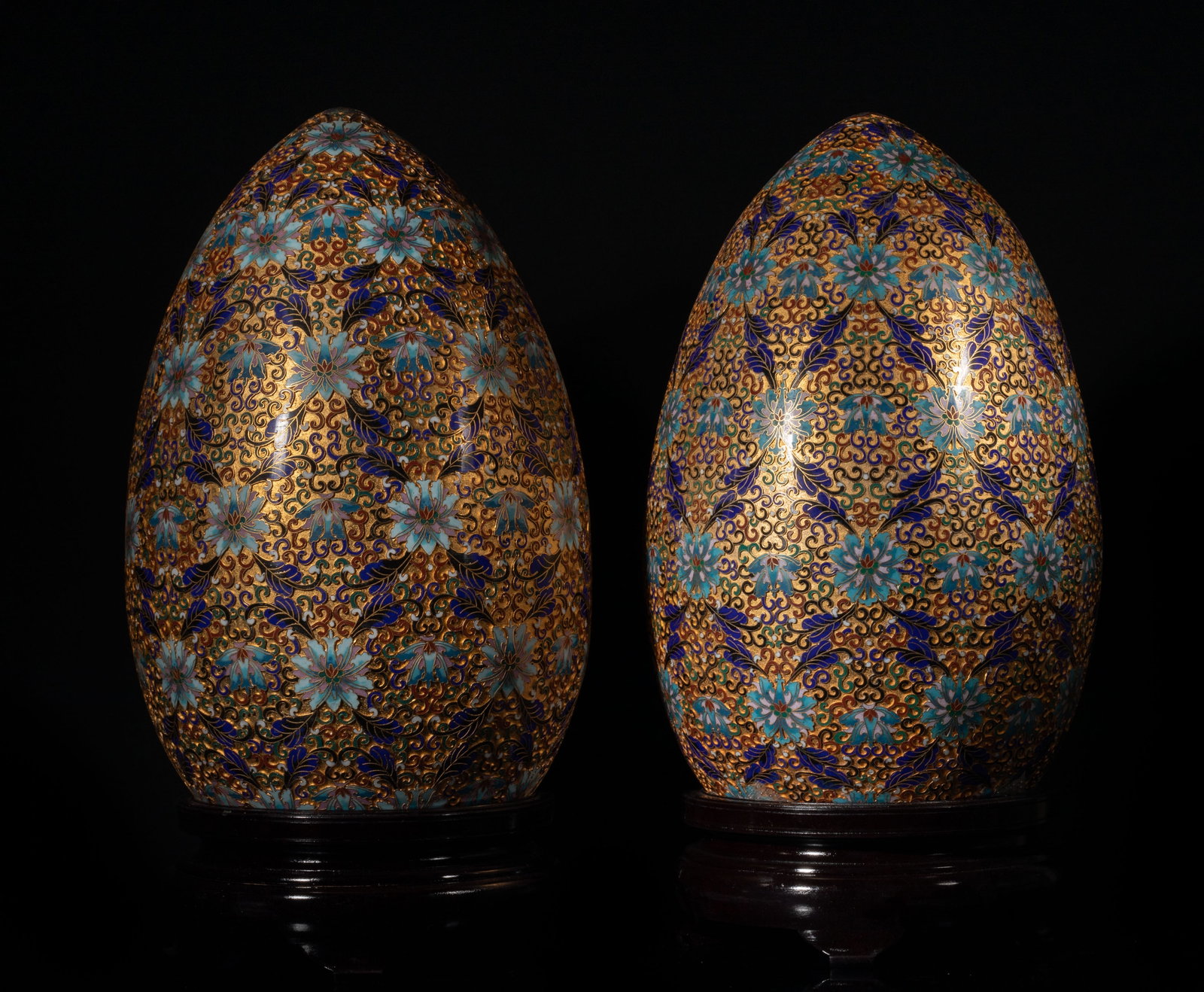 Two Massive Chinese Cloisonne Sculpture Eggs: A pair of massive Chinese cloisonne enamel sculpture eggs, detailed with floral and foliage pattern in vibrant blue and gold tones, each with a fitted wood stand. Approx. 22.8*11.8 inch (W/Stand)