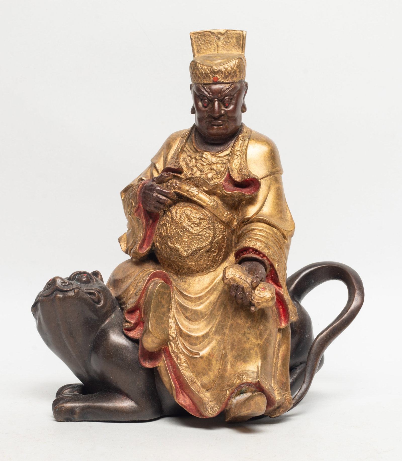 Unusual Chinese Export Bronze Buddha: The bronze buddha wearing a hat and layered robes, decorated with gold leaf and red trim, sited on a top of beast with a long curving tail. Approx. 7.4*8.8 inch