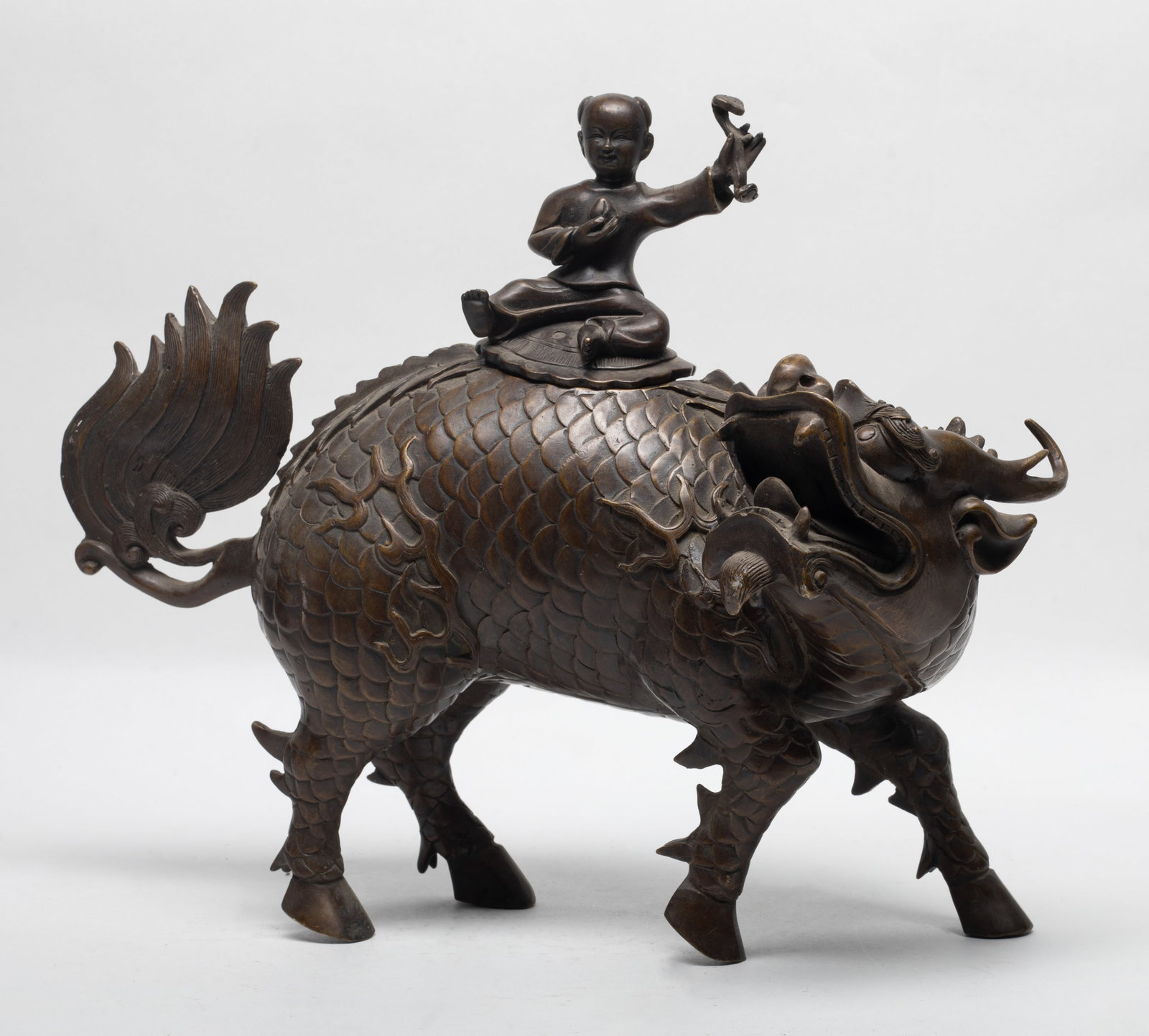 Rare Chinese Bronze Sculpture of Qilin: The crouching beasts with its head turned right, detailed with bulging eyes, protruding nose, and bushy hair, ending with a boy seated on the top of the beast, with left hand holding a ruyi. Approx. 1
