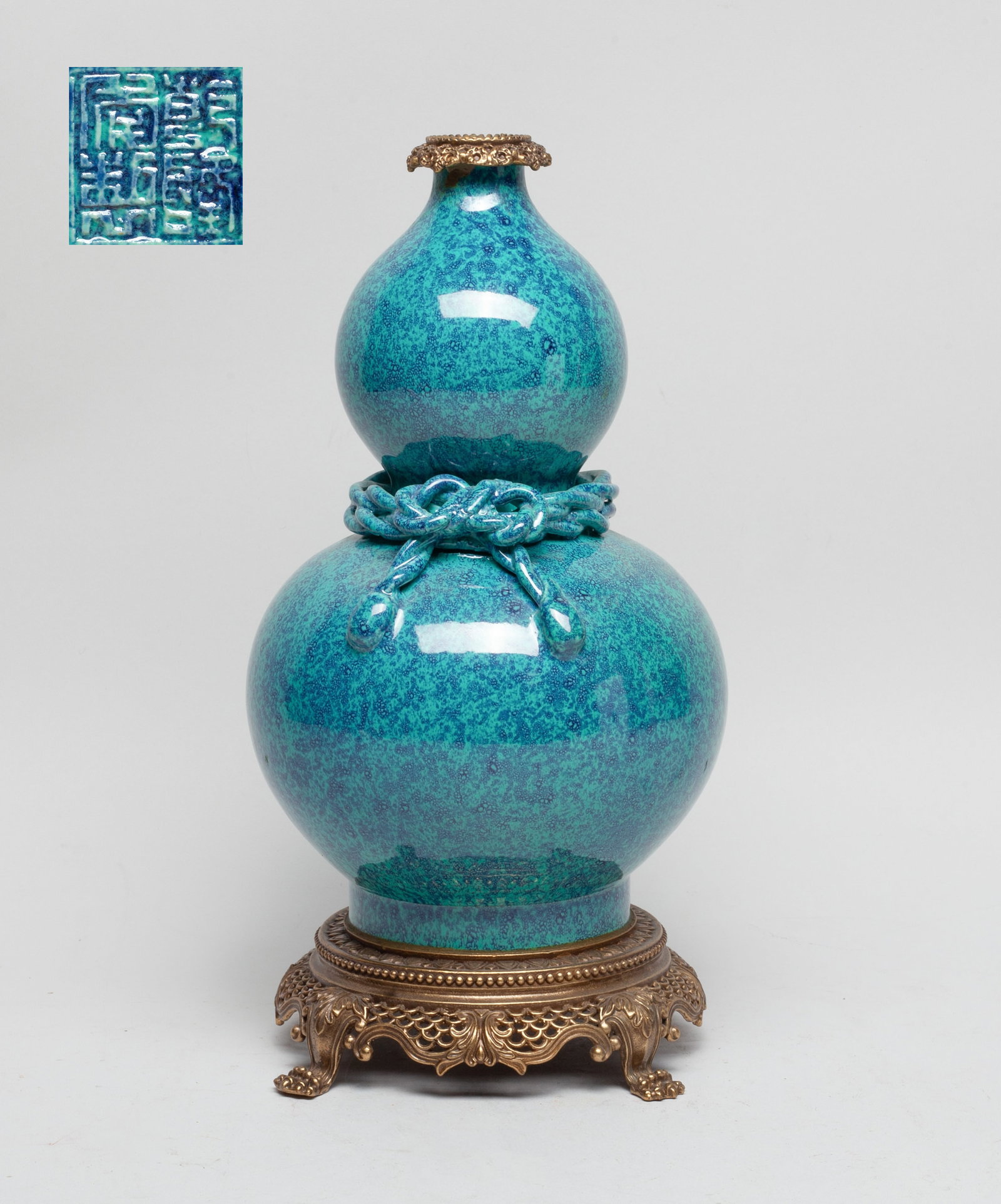 Chinese Export Flambe Glazed Porcelain Vase: Of double gourd form, the waist decorated with knotted ropes, overall covered with turquoise glaze suffused with dark-blue bubbles, set with metal mouth and foot, the bottom incised with a seal mark.