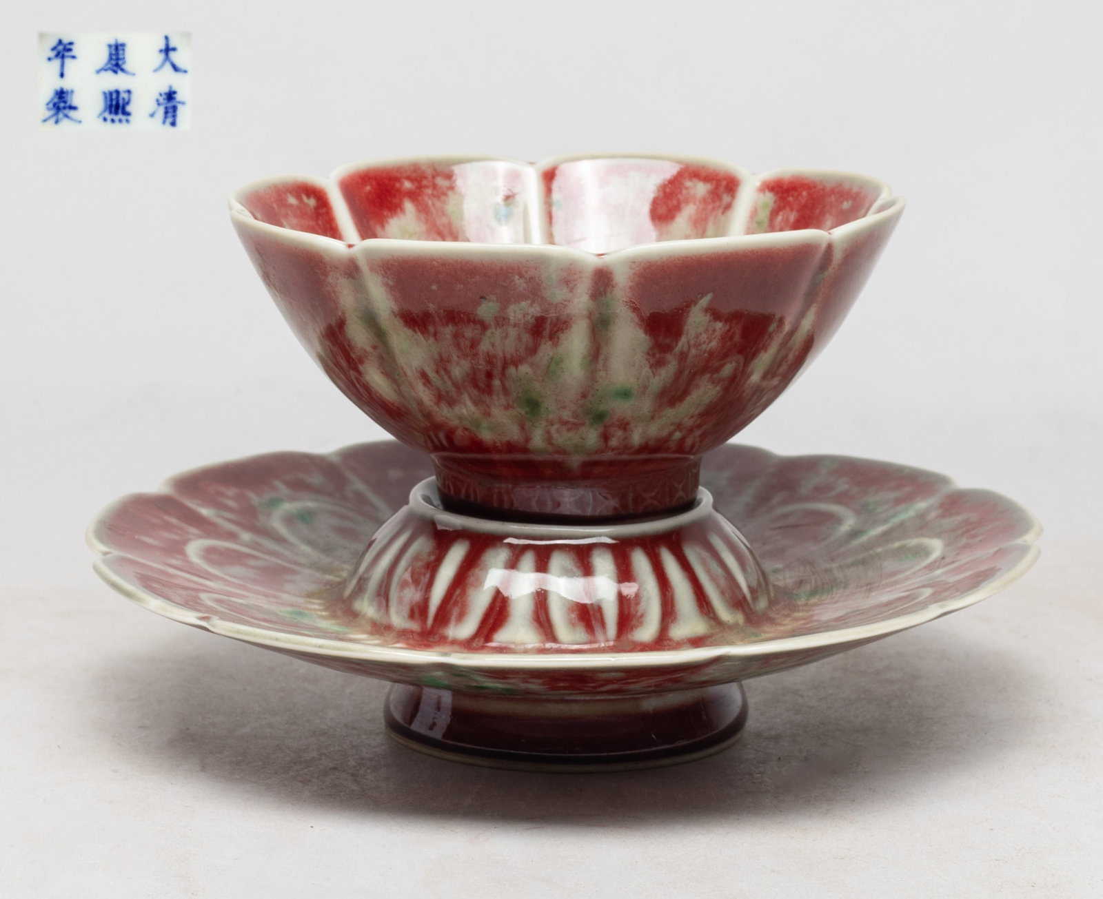 Rare Chinese Flambe Glazed Porcelain Tea Cup: The cup and stand molded of floral form, covered with copper red glaze suffused with green inclusions, the cup and stand bottom marked with six characters. Approx. 4.1*1.9 inch (cup size). The Estate