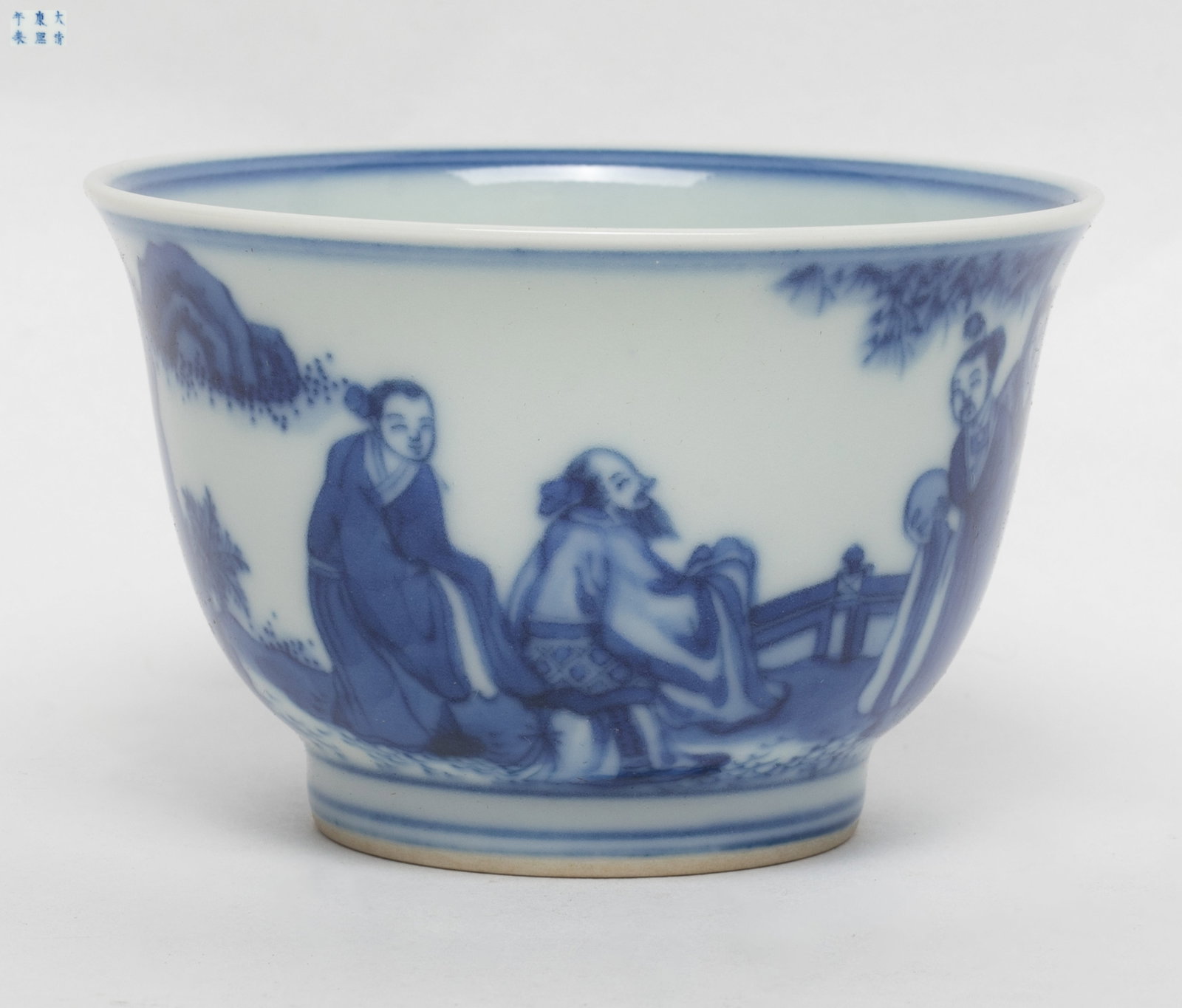 Chinese Blue & White Porcelain Tea Cup: The blue and white porcelain tea cup painted in cobalt blue with continuous landscape scene depicting figures talking under the pine tree, the base inscribed with a six-character within a double