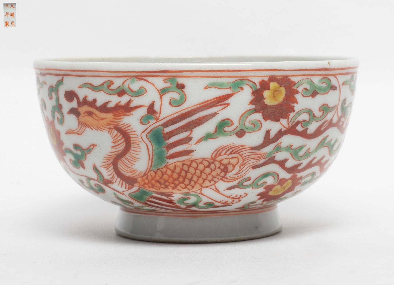 Chinese Export Porcelain Bowl: The bowl of deep rounded body with an everted rim and short ring foot, featuring overglaze iron-red floral scrolls and green accents, highlight with phoenix pattern, the base inscribed with a