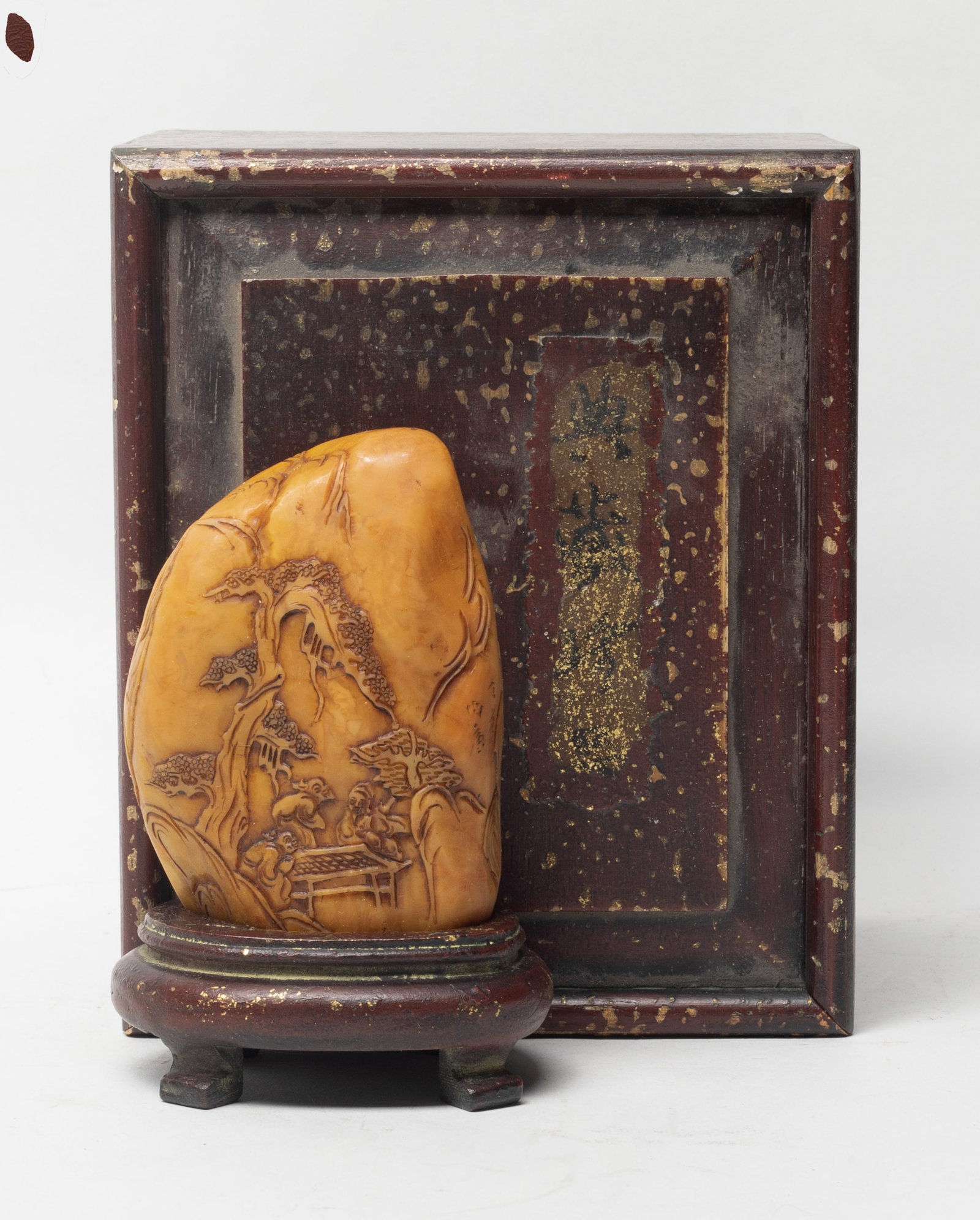 Chinese Shoushan Stone Carved Sculpture: Deftly carved in relief with continuous landscape scene detailed with figures hanging around under the pine tree among the mountain view, with a wood stand and case. Approx. 4.93*2.8 inch (w/stand)