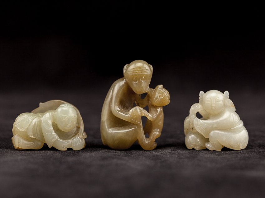 A Set Of Three Chinese Antique Carved Jades: A set of three carved jades; the white color jade carved as a seated boy playing with cat, the greenish-color with brown-suffusions jade carved as a reclining boy holding a big lily pad, the yellowish