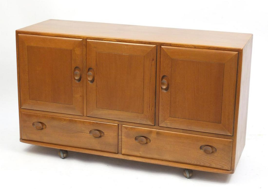 Ercol Windsor light elm sideboard with three cupboard: Ercol Windsor light elm sideboard with three cupboard doors enclosing an adjustable shelf and cutlery tray above two base drawers, 76cm H x 129.5cm W x 44cm D