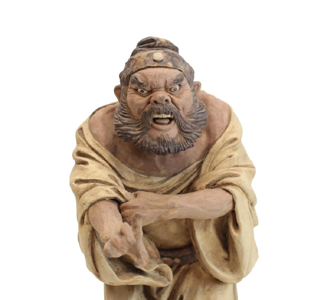 Chinese Shiwan Pottery Stoneware Warrior: Chinese Shiwan Pottery Stoneware Warrior Figurine, Fierce character, bearded and pulling up sleeve, sword hanging from his belt. Unglazed, with ocher colored robes. Unmarked. On wood stand 3.75.lbs. 8