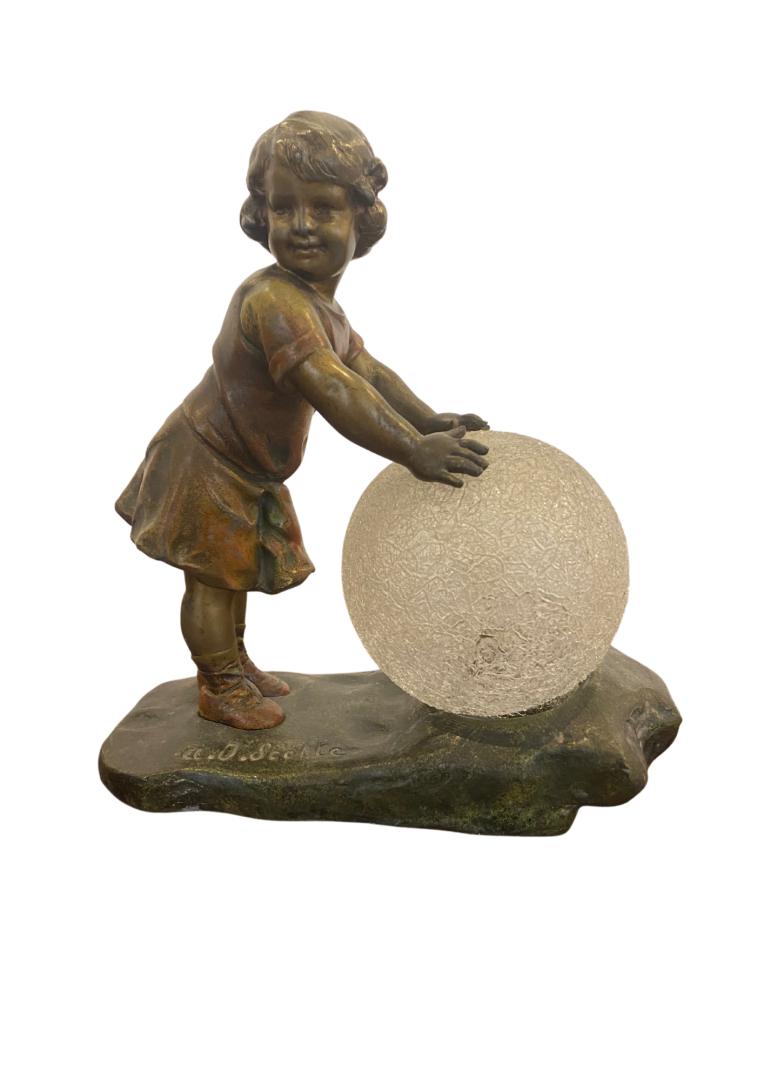 A.J. SCOTTE (1885-1905)Lampe en rÃ©gule Ã patine dorÃ©e, figurant une petite fille roulant une: A.J. SCOTTE (1885-1905)Lampe en rÃ©gule Ã patine dorÃ©e, figurant une petite fille roulant une balle SignÃ©e AJ ScotteCirca 1900Hauteur : 23cm