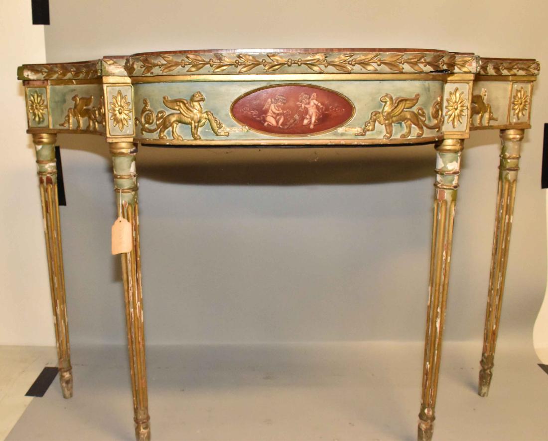 A GEORGE III STYLE GILT AND GRAY-PAINTED CONSOLE TABLE.: A GEORGE III STYLE GILT AND GRAY-PAINTED CONSOLE TABLE. 20th Century. With shield-shaped top and conforming apron applied with griffin and scroll carving, on fluted round tapering legs. 32 in. high; 4