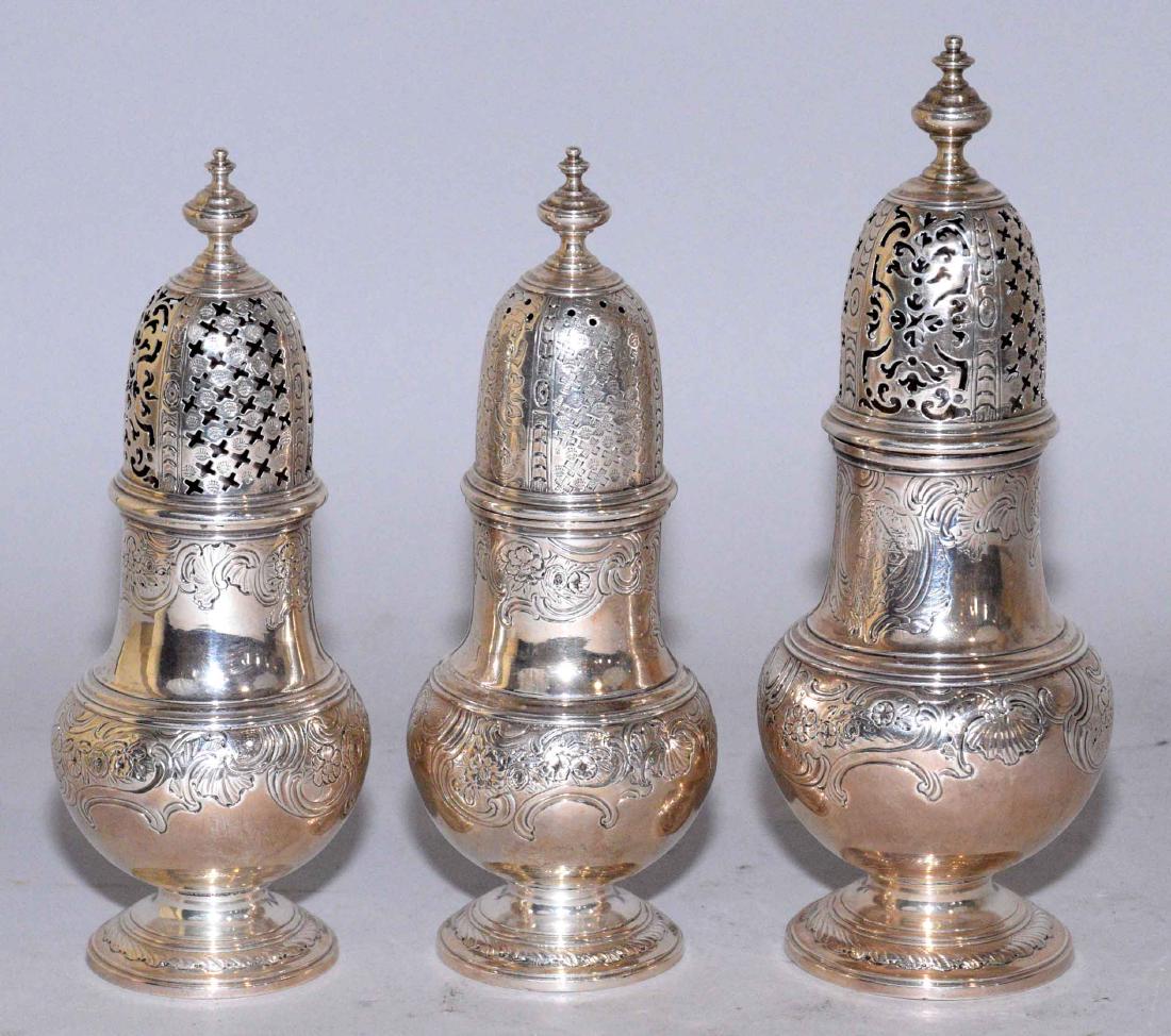 A SET OF THREE GEORGE II SILVER CASTERS. Mark of James: A SET OF THREE GEORGE II SILVER CASTERS. Mark of James Goodwin, London, 1741. Each of baluster-form, with pierced covers and flat-chased rocaille including: a pair, 6 1/2 in. high (each). A slightly l