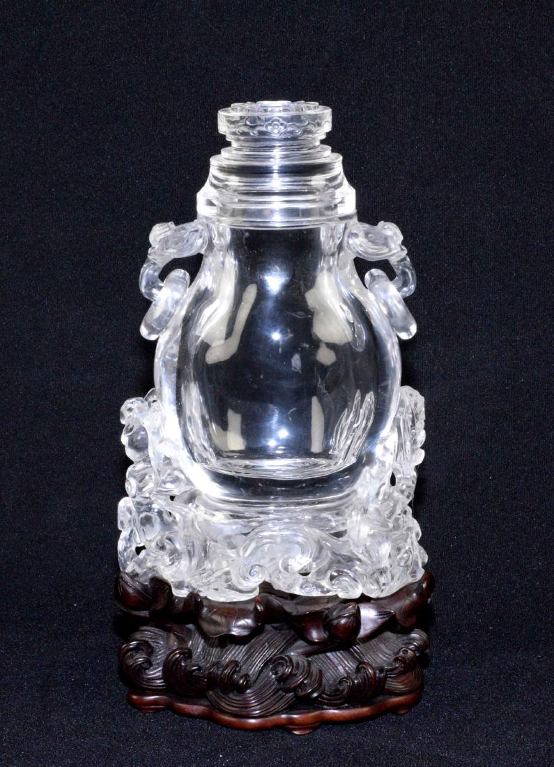 A CHINESE CARVED ROCK CRYSTAL VASE AND COVER. Late: A CHINESE CARVED ROCK CRYSTAL VASE AND COVER. Late 19th/20th Century. Of flattened pear-form, the sides with pendant ring and taotie mask handles, the base with trailing entwined tree trunks, 10 in. h