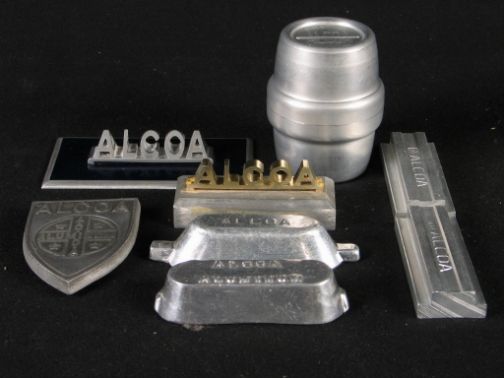 8 ALCOA ITEMS. Includes: (1) small shield Alcoa l: 8 ALCOA ITEMS. Includes: (1) small shield Alcoa logo c. 1943, 3 1/2''H. (2) small aluminum ingots, 3 1/2''L, 4''L. (2) aluminum rail samples, 3 1/8''L. (2) Alcoa logo desk decorations, 3 1/4''W, 4 1/2