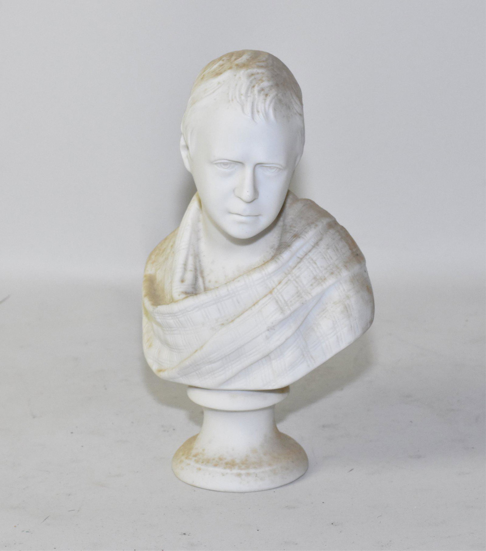 PARIAN PORCELAIN BUST - A draped bust of a: PARIAN PORCELAIN BUST - A draped bust of a gentleman. Raised on a base. 9" high. Note: Some small green algae growth from having resided out of doors recently.