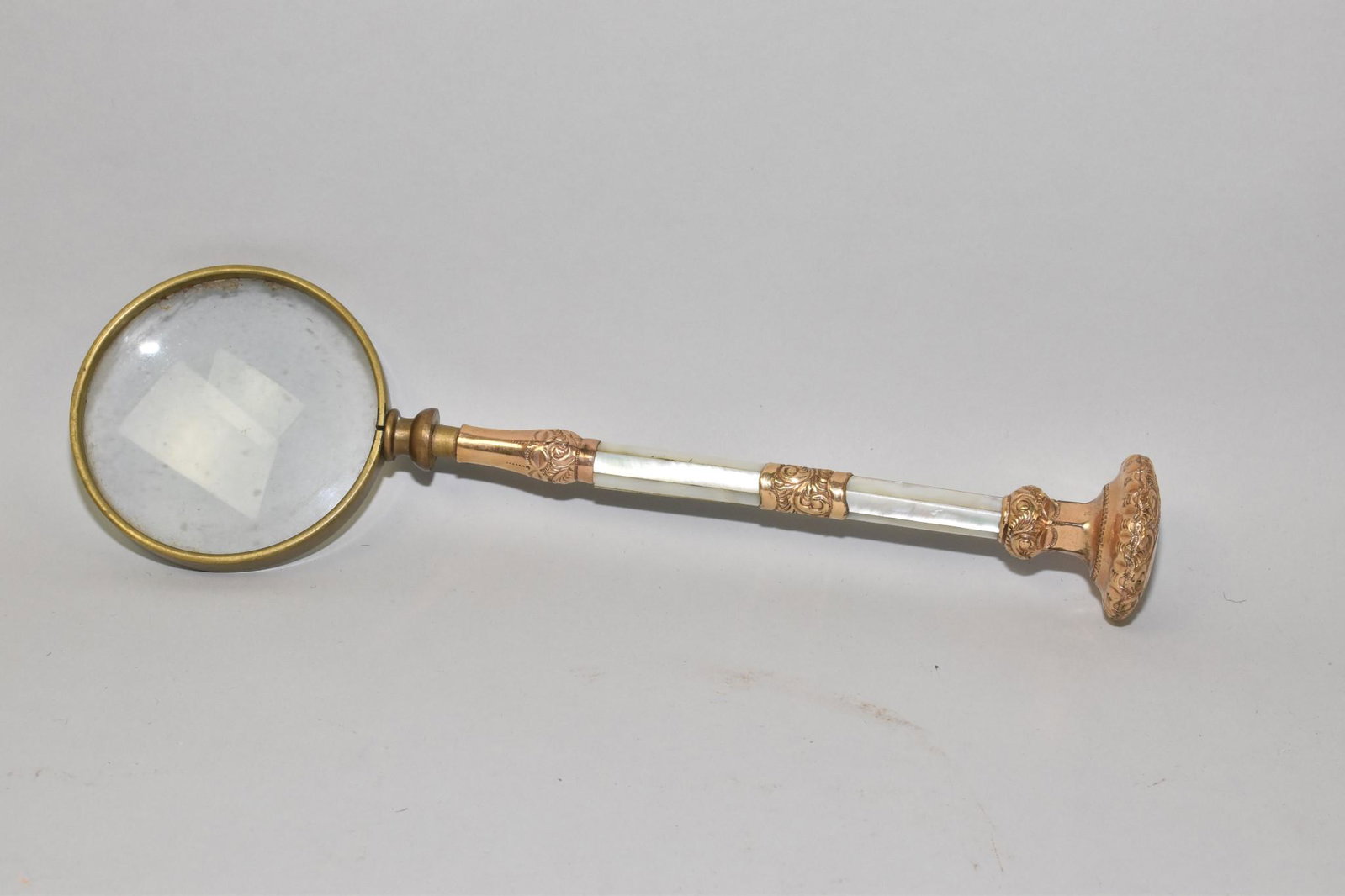 MAGNIFYING GLASS -The 8" handle of gold plate: MAGNIFYING GLASS -The 8" handle of gold plate and mother of pearl; the finial of the handle is engraved: "Mrs. Sarah McCausland". Overall: 12.5" l.
