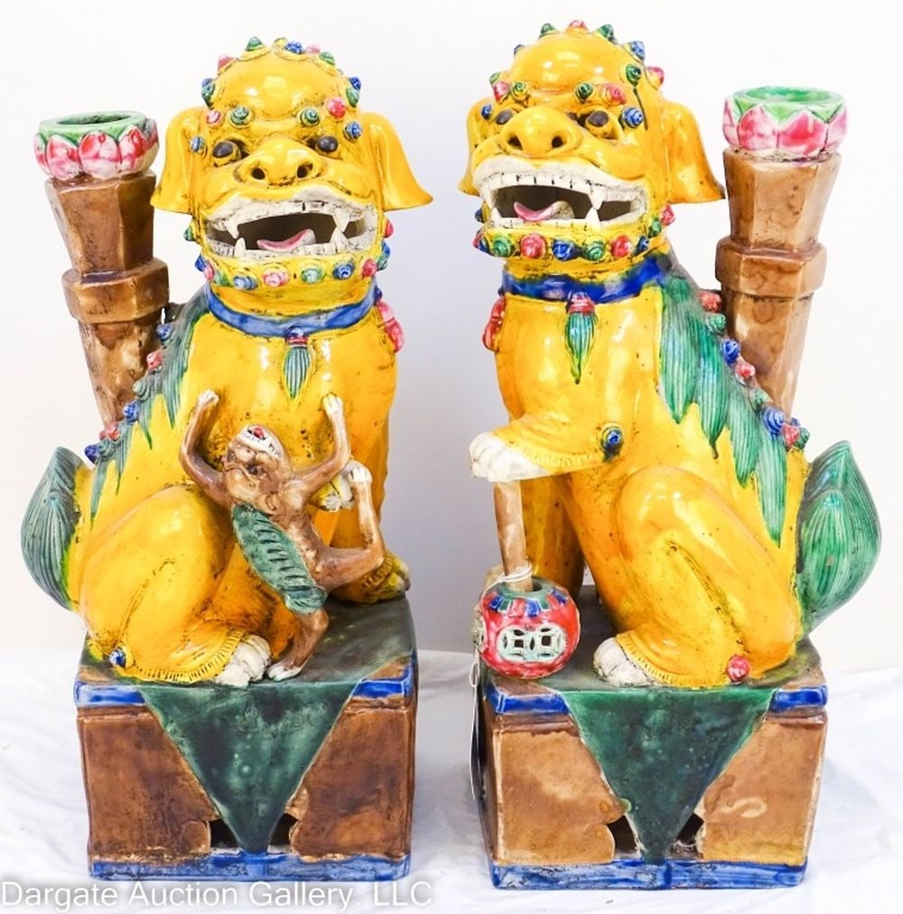 PAIR CHINESE FAMILLE JAUNE ET VERTE FOO DOGS: Pair Chinese Famille Jaune et Verte Foo Dogs - Porcelain foo dogs sitting on plinths. One has a ball that moves on its stick, the other is holding a monkey. Both have incense burners sitting behind th