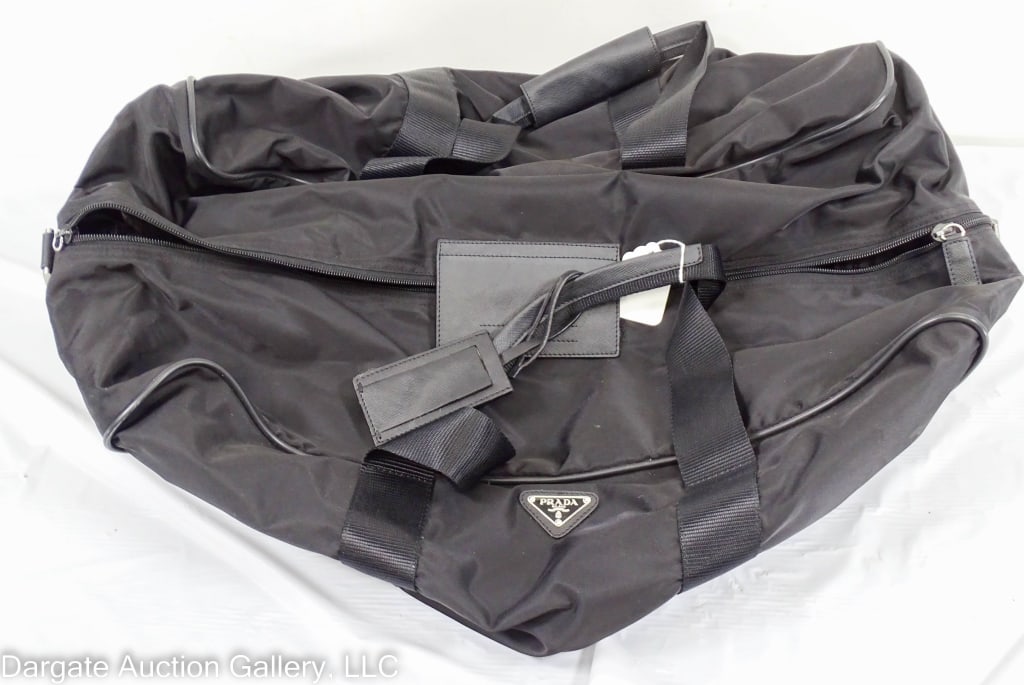 PRADA BLACK DUFFEL TRAVEL BAG: Black nylon and leather / Measurements: Approx: 14"H x 26"W 13"D / Condition: Appears to never have been used / leather tag on one zipper is missingDISCLAIMER: ****WHILE THE DESIGNER ITEMS IN OUR SALE