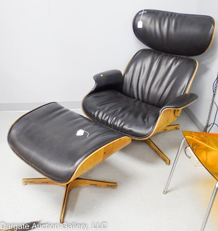 PLYCRAFT EAMES CHAIR & OTTOMAN: Black leather swivel lounge chair and matching ottoman, both with wood clad bases / Playcraft label / Chair - 39"H x 31"W x 32"L , Ottoman - 18"H x 25"W x 20"D / Condition: Needs cleaned