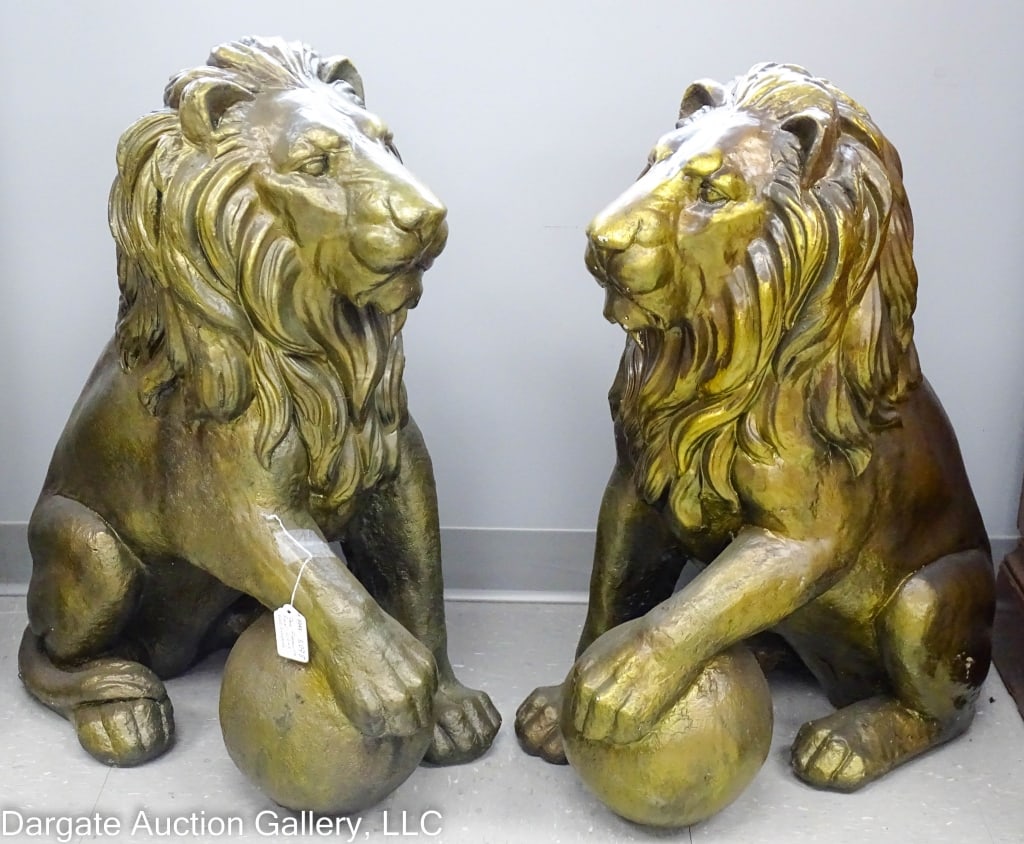 2 FIBERGLASS REGAL LIONS STATUES W/BRONZE FINISH: A pair of hollow fiberglass statues of gatekeeper lions, with one paw resting on a ball. Bronze finish, with slight wear to the finish on one lions face, showing more of a gold tone. / Measures: 32" x