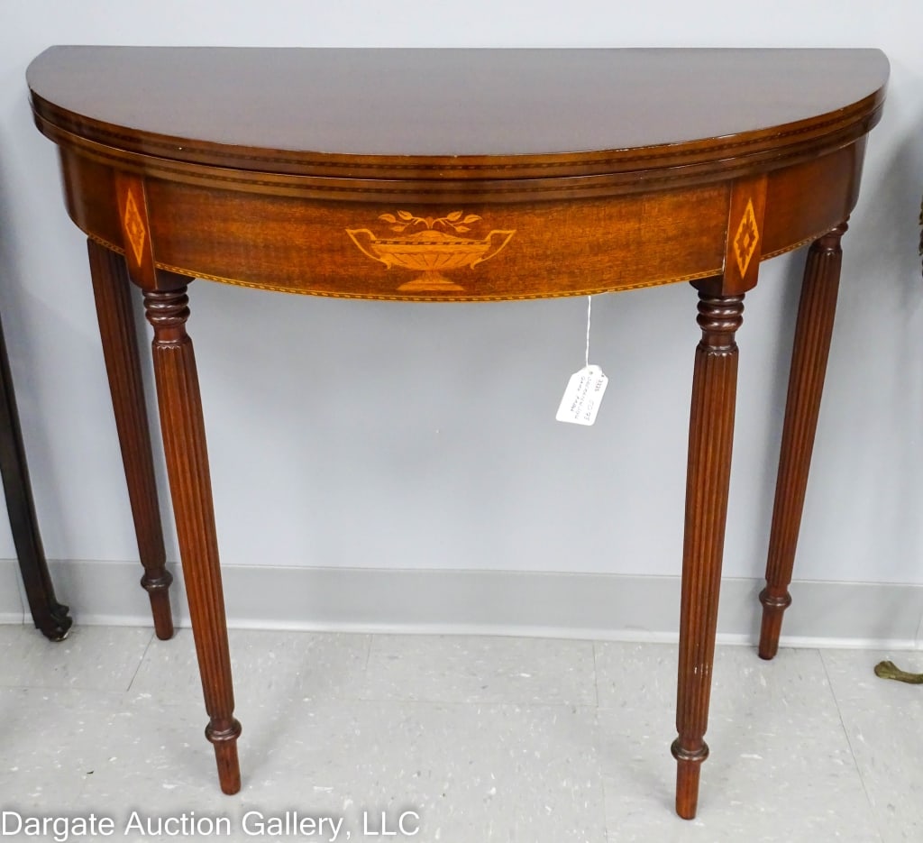 SHERATON STYLE DEMILUNE MAHOGANY GAME TABLE: A 20th C. Sheraton style mahogany game table inlaid with a urn and floral motif in the center of the the apron. Diamonds inlaid on the top of the reeded legs and banding on edges. Swing out gate legs 