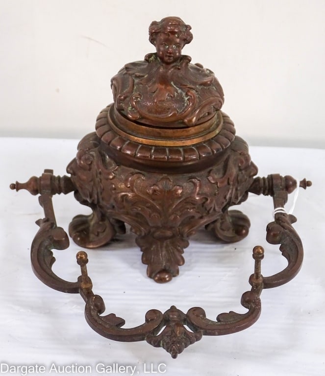 BRONZE INK WELL PEN HOLDER NORTH WIND FACES: Very nice bronze Victorian style ink well holder with 2 North Wind faces holding the pen holder on sides. Cherub head on lid. Porcelain ink well with gold trim. / Measures: 5.75H" x 6.5W" x 6D" / Prov