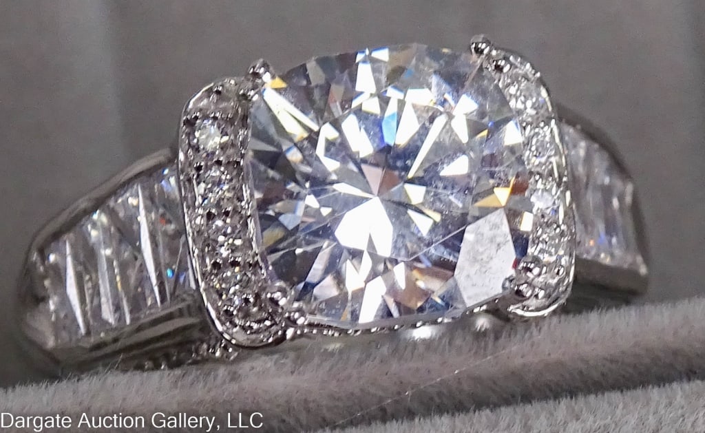 14K GOLD CUBIC ZIRCONIA COCKTAIL RING: White gold cocktail ring set with a round cubic zirconia, the flank sides of the round stone have a row of smaller CZ stones. Each panel on the side has an emerald cut, and the flanks are set with gra