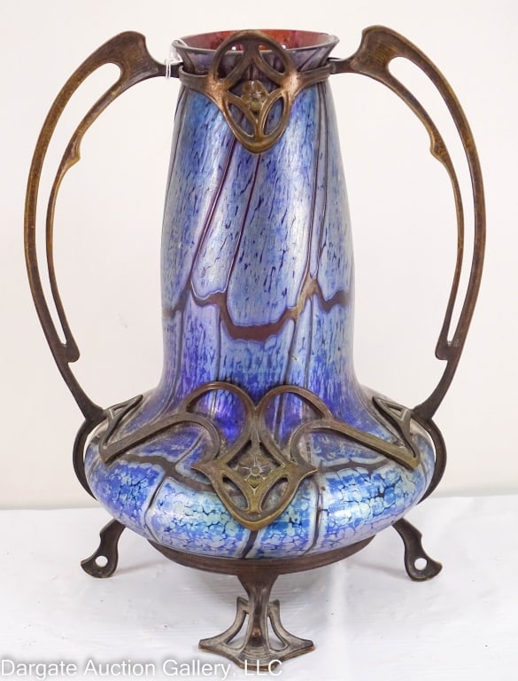 LOETZ VASE IN A PATINATED BRONZE HOLDER: Purple Loetz vase with a blue iridescent finish in an Art Nouveau bronze mount. Not marked. / Measures: 12"H x 9.5"Wx8"D / Condition: 3 chips to the rim