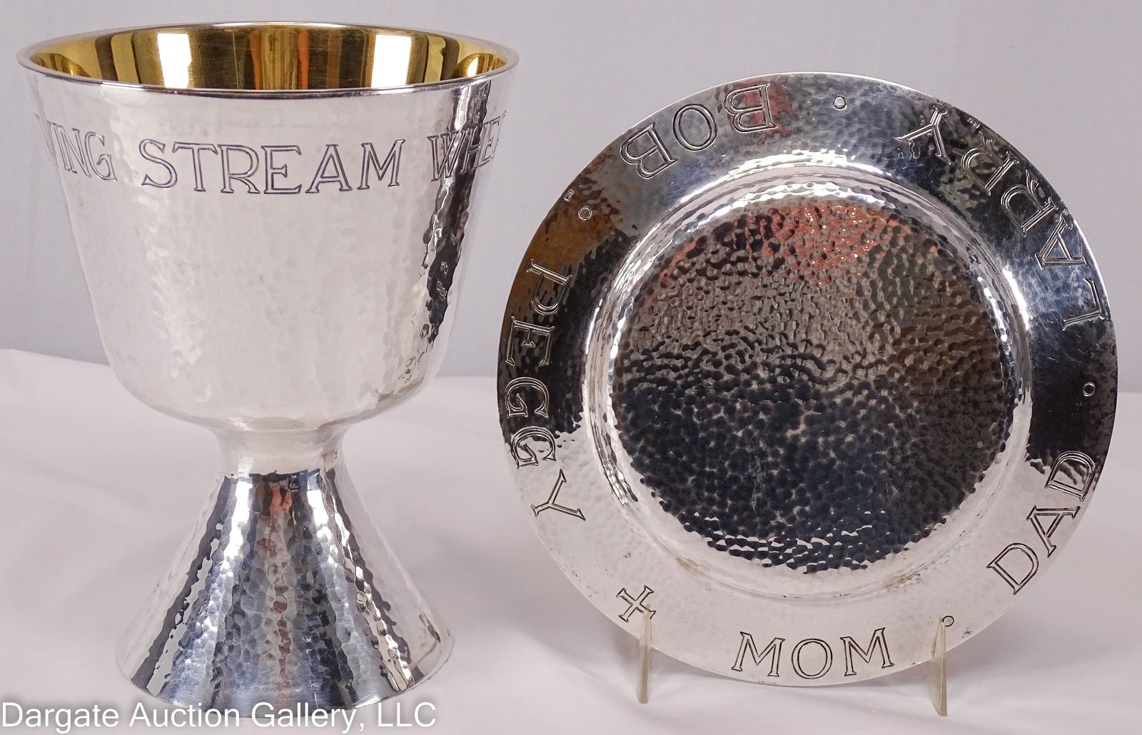 ADRIAN HAMERS STERLING CHALCE COMMUNIOT SET: A Sterling chalice and paten set in a velvet lined case, retailed by Adrian Hamers. Both pieces marked [925]. Chalice is weighted with a cross in the base, and inscribed across the top [A LIVING STREA