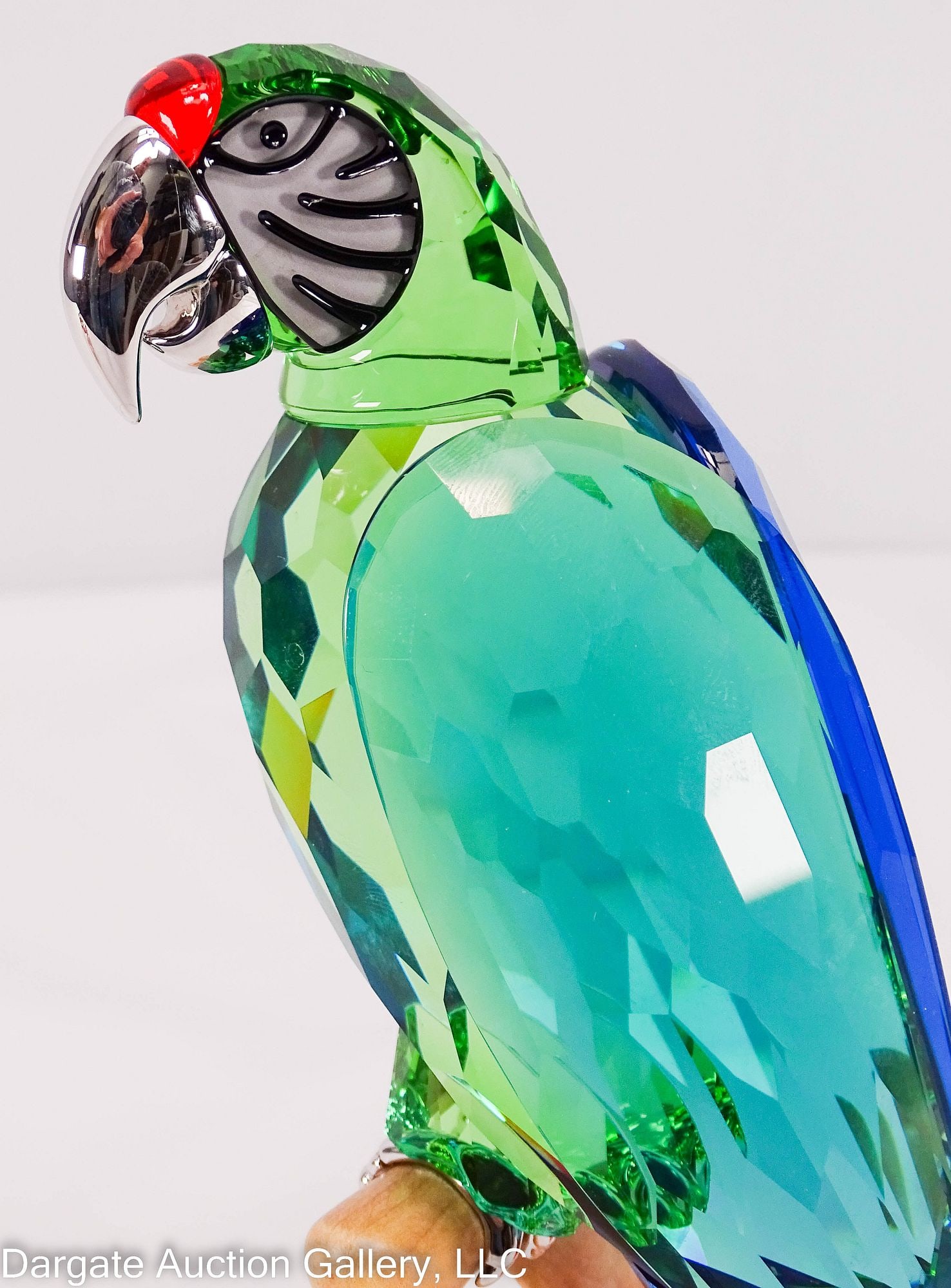SWAROVSKI CRYSTAL PARADISDE BIRDS GREEN MACAW: 2005 (Retired 2011) Designed by Roland Schuster; a faceted figure of a green macaw from the Paradise Birds Collection, perched on a wood base, with chrome accents; Swarovski acid etched mark on tail; 