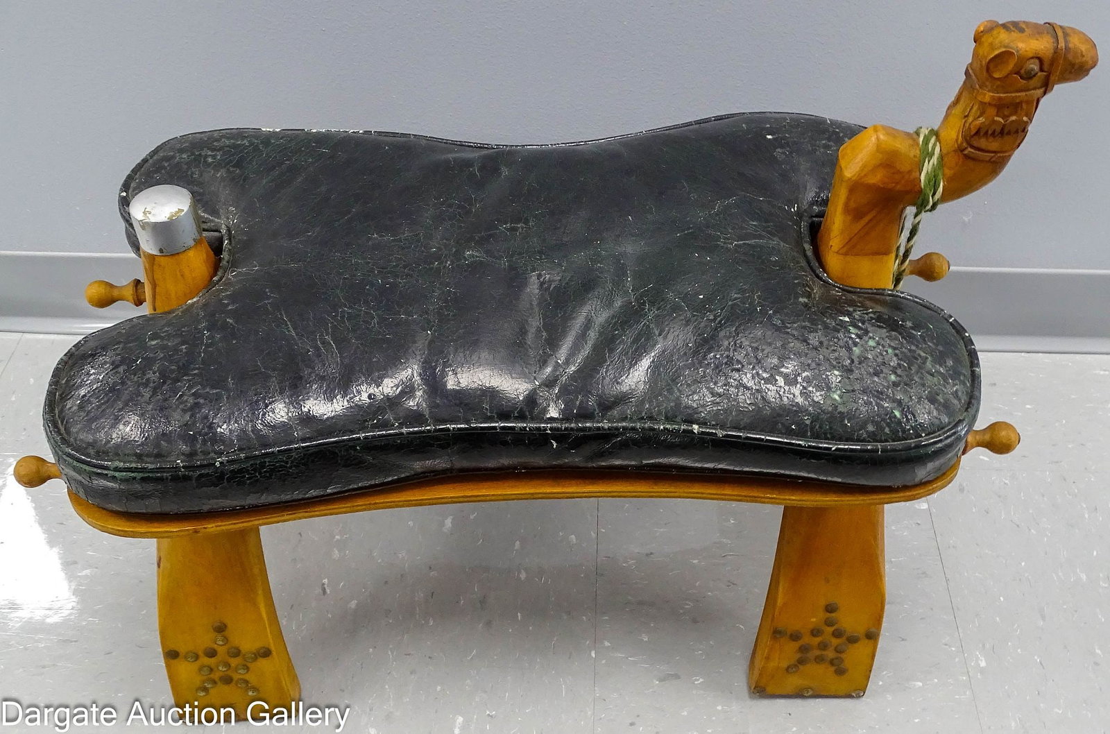 EGYPTIAN WOODEN CAMEL SADDLE STOOL: Mid-Eastern Mid-20th Century camel saddle stool with dark green leather seat, carved camel head pommel with brass bell; Measures: 20"H x 15"W x 28"D; Condition - Leather seat shows wear and cracks; we