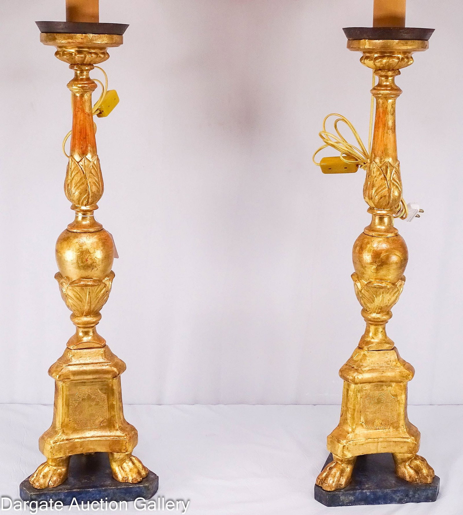 PAIR OF OVERSIZED PRICKET CANDLESTICK LAMPS: A pair of carved wooden continental gilt wood pricket candlesticks that have been electrified; Triangular bases painted to look like blue marble with [P.A.R.] painted on fronts, carved paw feet, with 