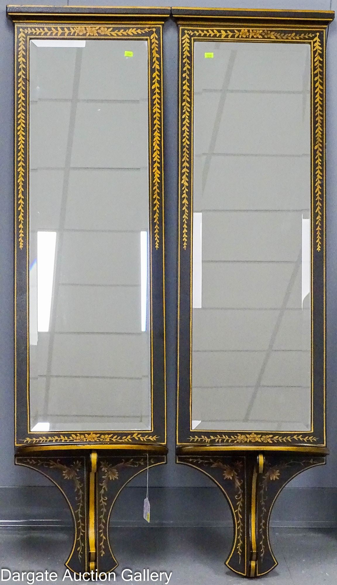 PAIR OF BLACK LACQUERED MIRRORED WALL SHELVES: A tall pair of beveled glass mirrors in black lacquer frames featuring demilune shelves. Hollywood Regency inspired style with hand-painted gold accents / Dimensions: 53" H x 15.