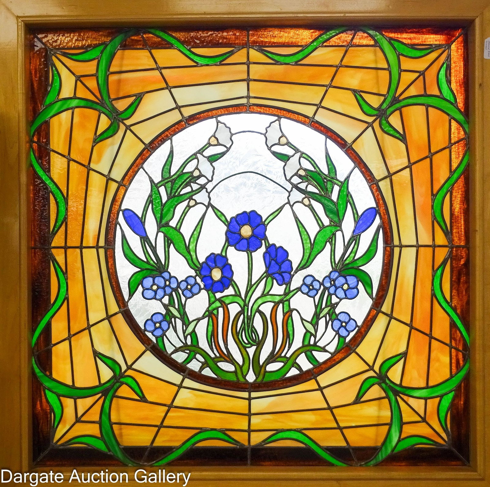 LARGE FLORAL STAINED GLASS WINDOW IN A BIRCH FRAME: A wood framed stained glass window with a caramel slag and green glass border, with a central circular design element of blue and white flowers among green foliage; Measures: Overall - 52.75"H x