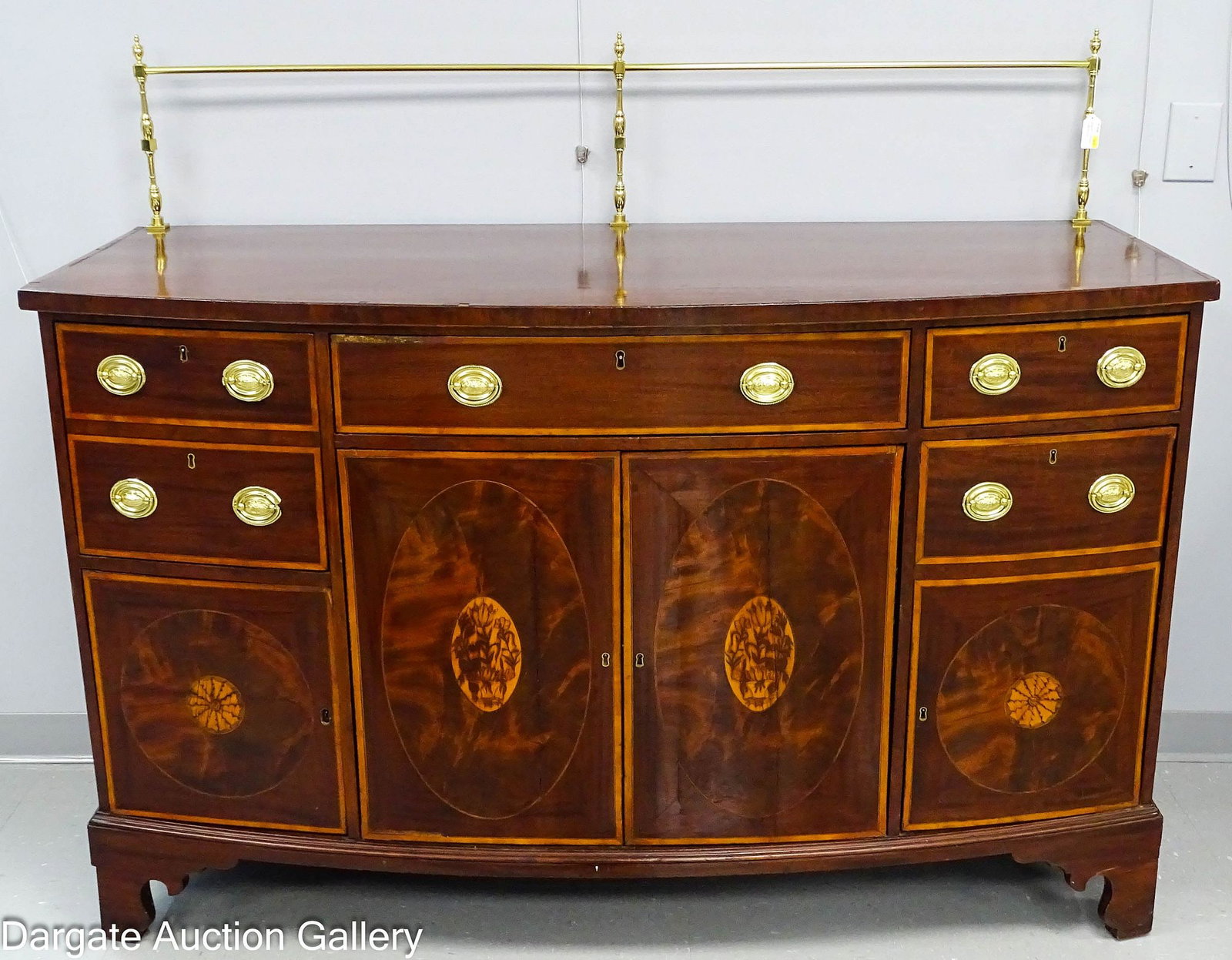 GEORGIAN INLAID MAHOGANY SIDEBOARD CIRCA 1810: A Georgian period mahogany sideboard featuring satinwood inlay and a modern replacement brass gallery. The piece includes a bow-front configuration with drawers and cabinets accented by inlaid reserve