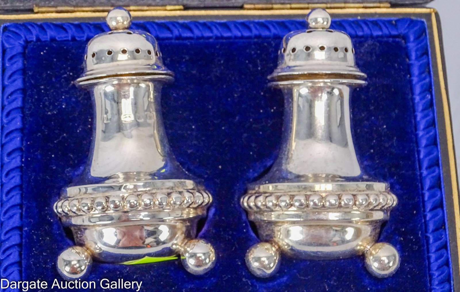 CASED STERLING SALT AND PEPPER SHAKERS: A cased set of English sterling salt and pepper shakers, bell form with beaded girdle and three ball feet hallmarked for [Birmingham, Sterling, 1897]. In a fitted velvet and silk lined box marked for 