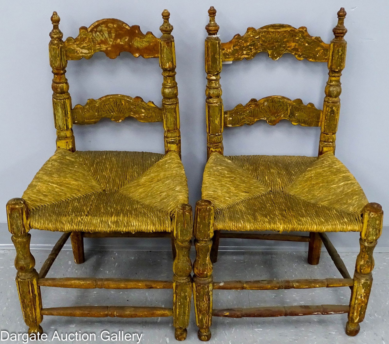 PAIR SPANISH COUNTRY STYLE LADDER BACK CHAIRS: A pair of low ladder back Spanish country style chairs featuring hand-woven rush seats and remnants of a heavy glazed finish. The back slats exhibit a carved design within the glazed finish. /