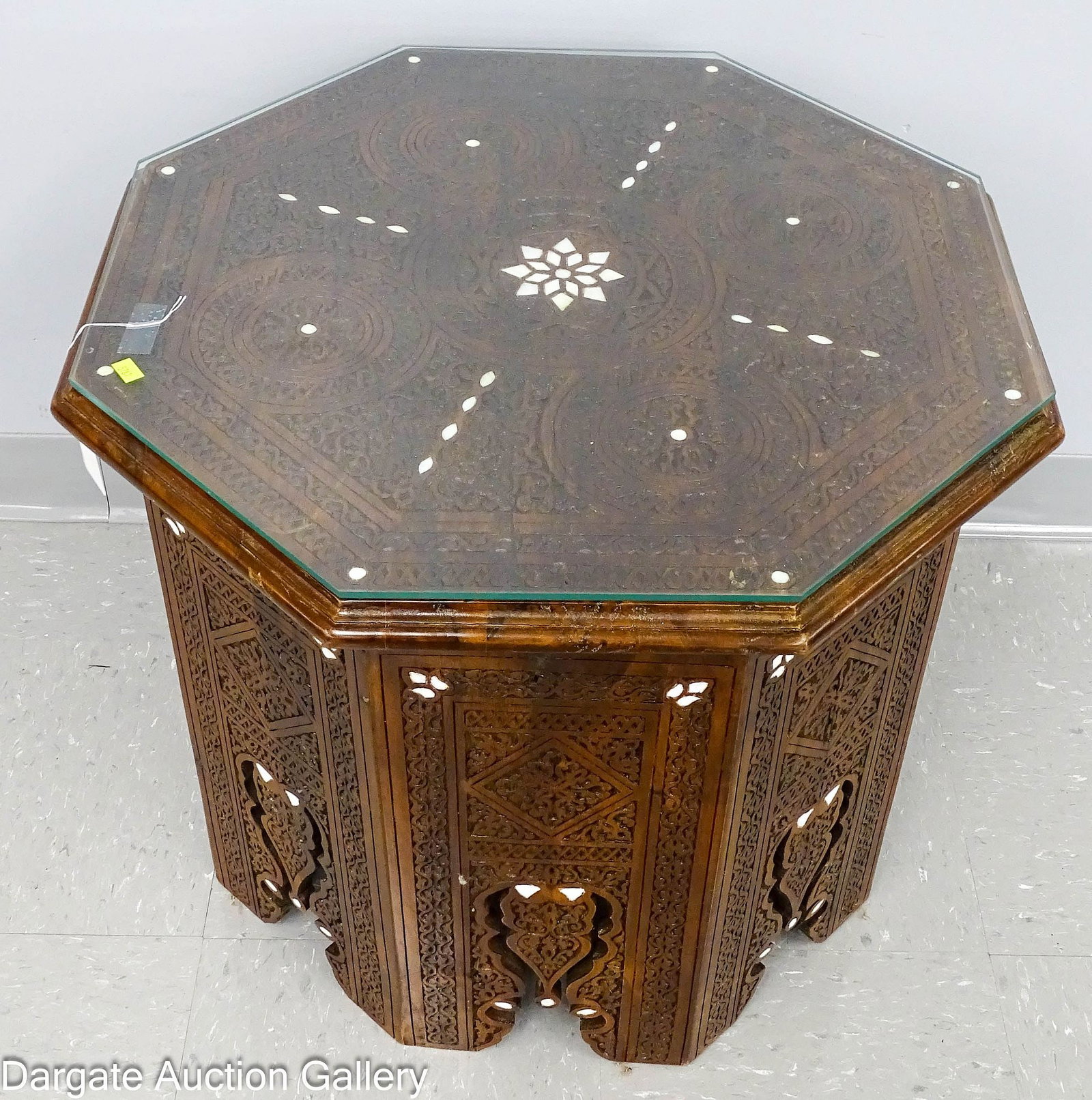 OCTOGANAL MOROCCAN TABLE with MOTHER OF PEARL INLAY: A Teakwood table, pierced and carved in the Moorish style with mother of pearl inlays on top and sides, with a glass top; Measures: 21"H x 24" diameter; Condition: Some minor scuffing and we