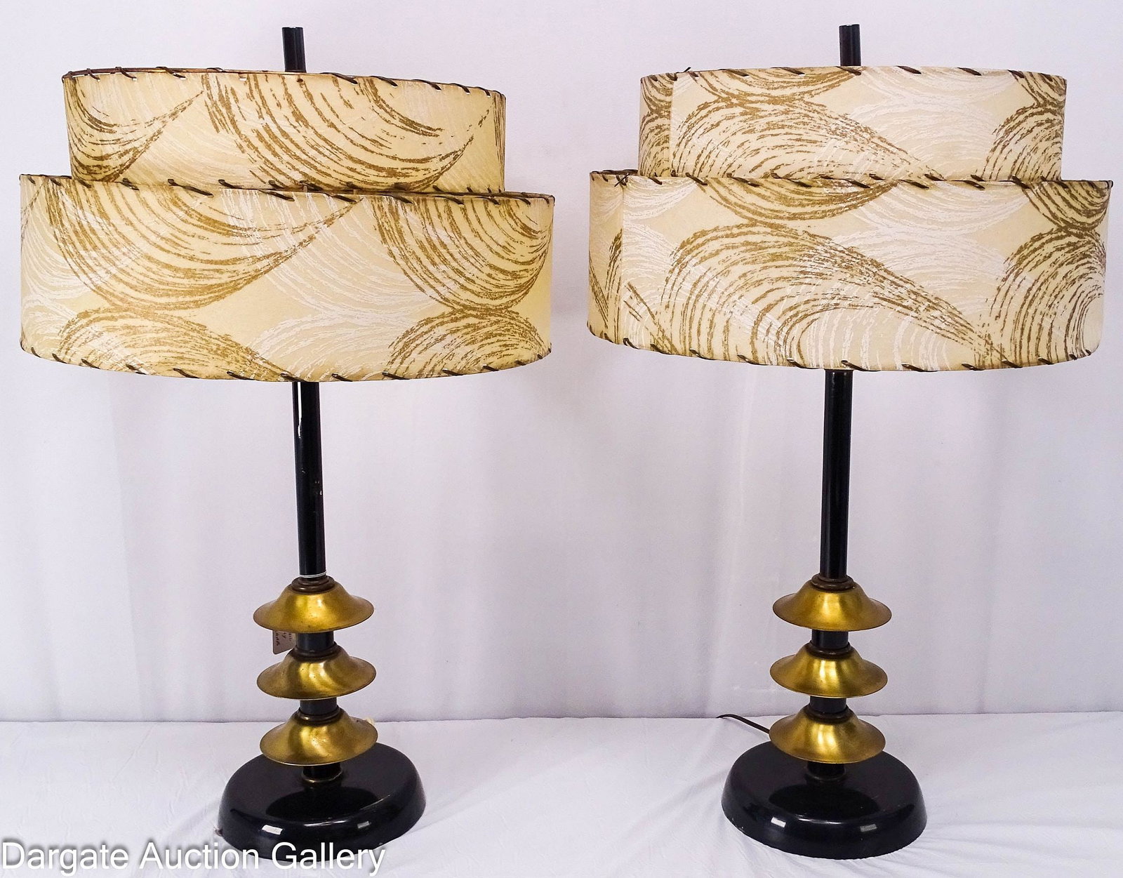 PAIR ATOMIC MID-CENTURY MODERN BLACK &BRASS TABLE LAMPS: A pair of mid-century modern black enamel on steel and brass table lamps in the atomic style, featuring original two-tiered pattern fiberglass shades with rawhide style stitching / Dimensions: