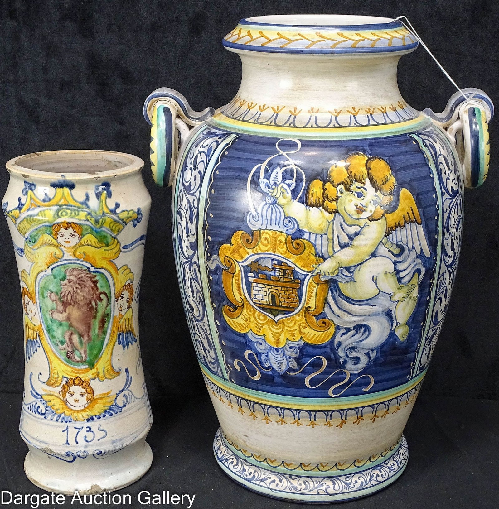2pcs DECORATIVE DERUTA STYLE POTTERY: Includes: A 13.25"H x 10"W armorial style vase with a cupid and ring handles, and a 9.5"H apothecary jar style armorial vase with putti, a lion and 1735; with artifically made chipping