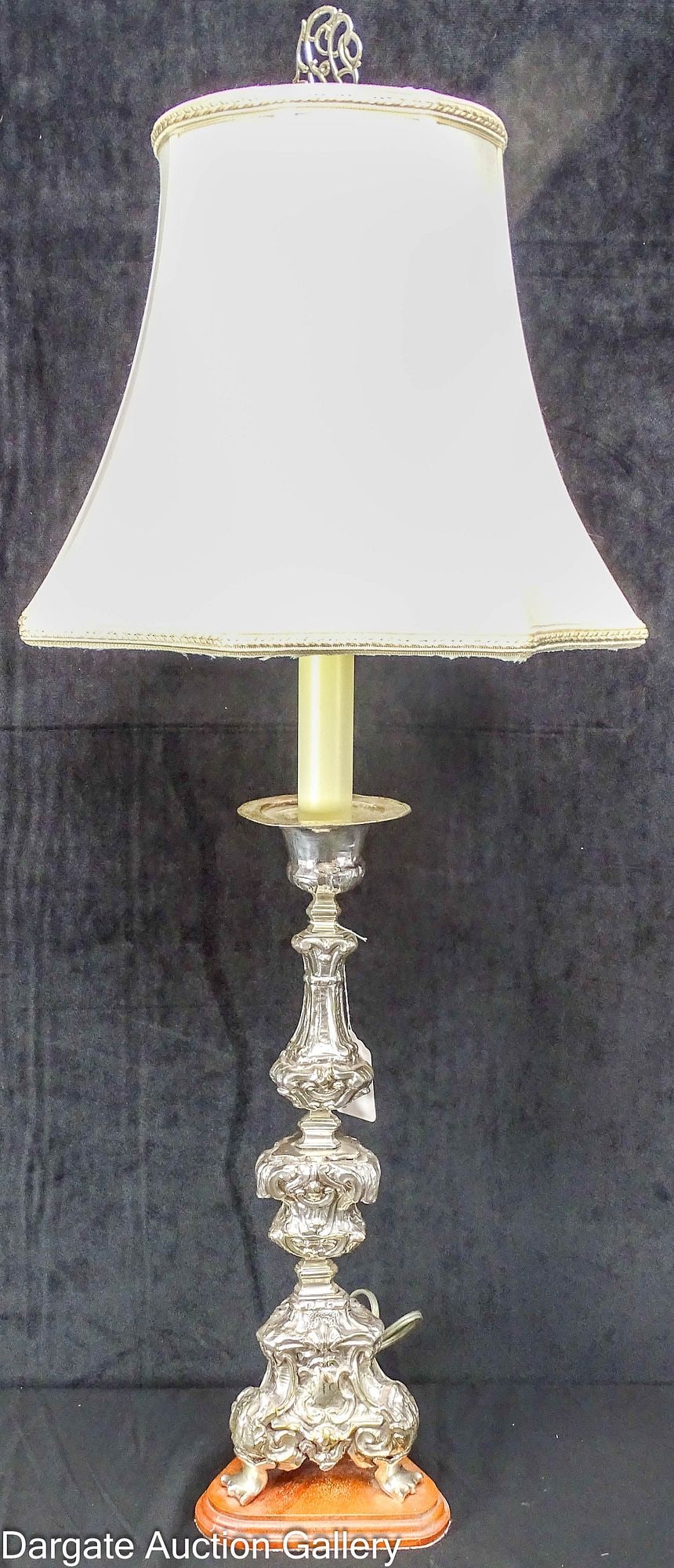 BAROQUE STYLE SILVERPLATE ALTAR CANDLESTICK LAMP: A baroque style silverplate alter candlestick, mounted on a wooden base and electrified by Kleins Fox Fire Gallery, Erie, PA; Scalloped octagonal fabric lamp; Measures: 25"H to light, 6" tri