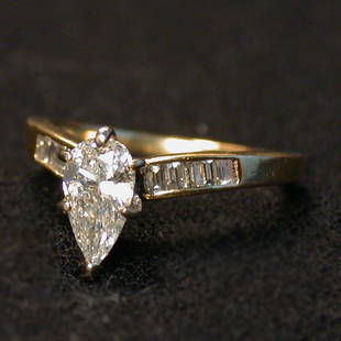 PEAR-SHAPED DIAMOND SOLITAIRE. The .65: PEAR-SHAPED DIAMOND SOLITAIRE. The .65 plus center stone is flanked on both sides by emerald cut stones mounted in a 14k gold setting. Color: G. Clarity: SI/2. Condition: no visible defects.