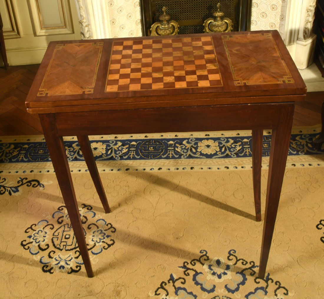 Mobilier Ancien: TABLE A JEUX en bois de placage dcor marquet d'un damier et de papillons. Le plateau de forme rectangulaire est escamotable. Elle repose sur quatre pieds gaines. Dbut XIXe sicle. H : 76 cm l : l72
