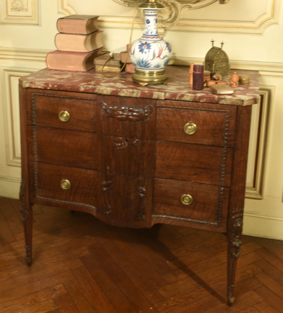 Mobilier Ancien: COMMODE de forme rectangulaire en bois naturel sculpt dcor d'une peau de lion. Elle ouvre trois tiroirs en faade. Montants pans cannels. Dessus de marbre rouge vein blanc. Fin XIXe sicle (ent