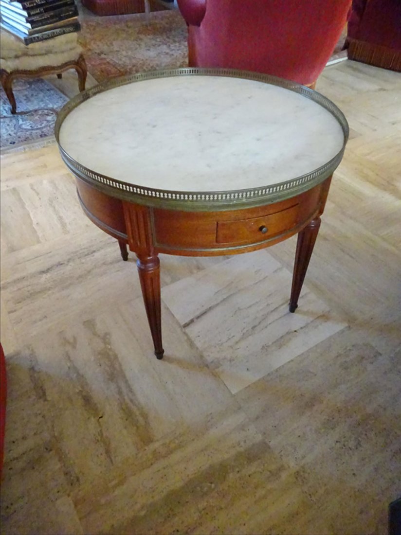 Mobilier Ancien: TABLE BOUILLOTTE en bois de placage reposant sur quatre pieds fusels et cannels ; la ceinture ouvre par deux tiroirs ; dessus de marbre blanc cercl d'une galerie en laiton. Travail du XIXe sicle.