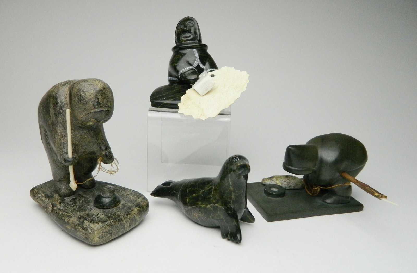 4 Inuit stone carvings: 4 Inuit stone carvings 1). Izasie Kopalie / Artic Bay- Iqaluit- Fisherman. 4 7/8''; 2 & 3). Johnny Manning / Cape Dorset- Woman Scraping Skin- signed. 3 1/4''; and Seal. 2 3/4''; 4). Johnassie Tukalla