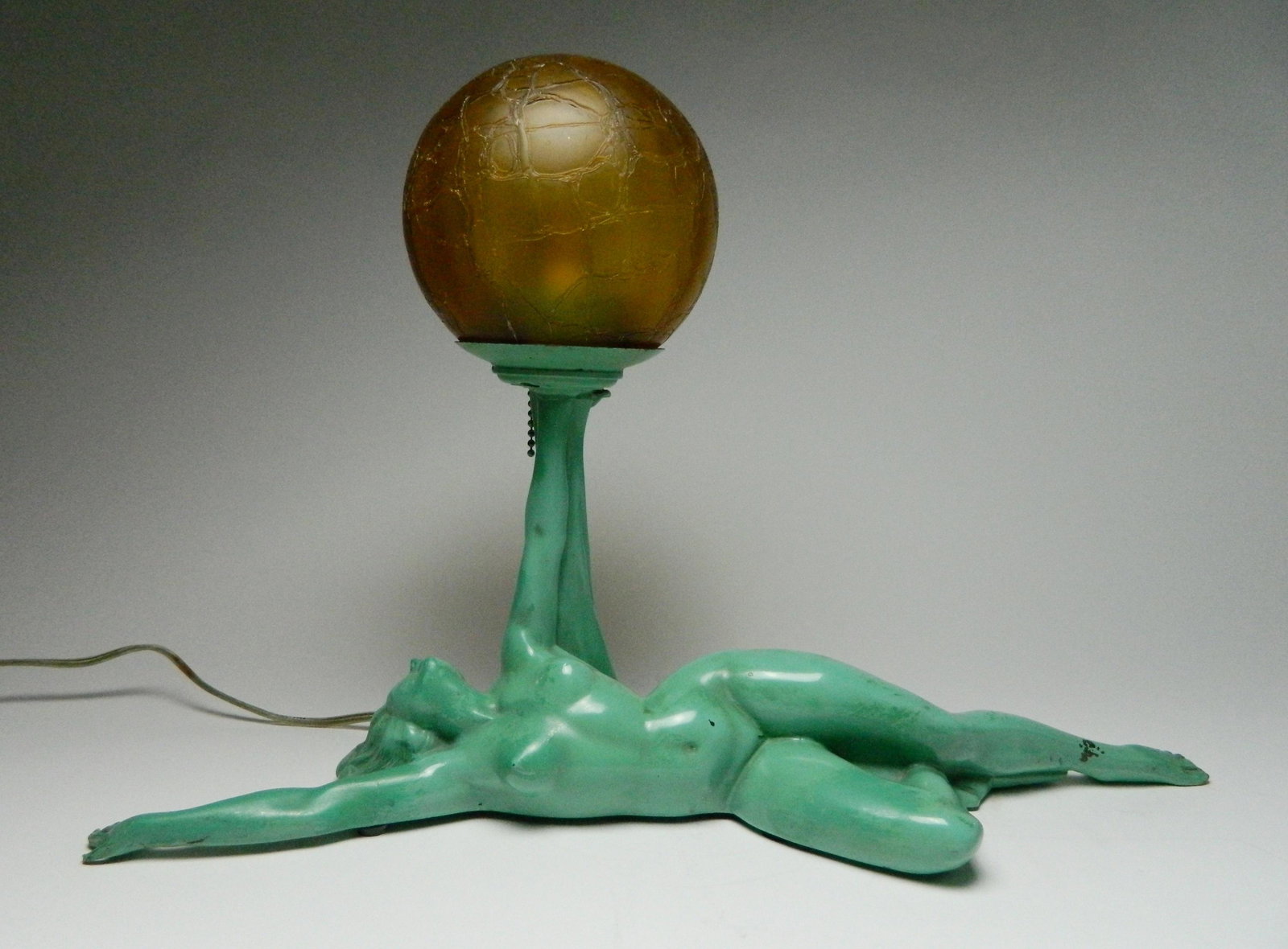 Aronson nude lamp: Aronson / Ronson AMW Reclining Nude Lamp in green, ca. 1910-20's, with original amber crackle glass ball shade, repaired hairline fracture of right arm. 11 1/2 x 18 x 6''. The now Ronson Company, orig