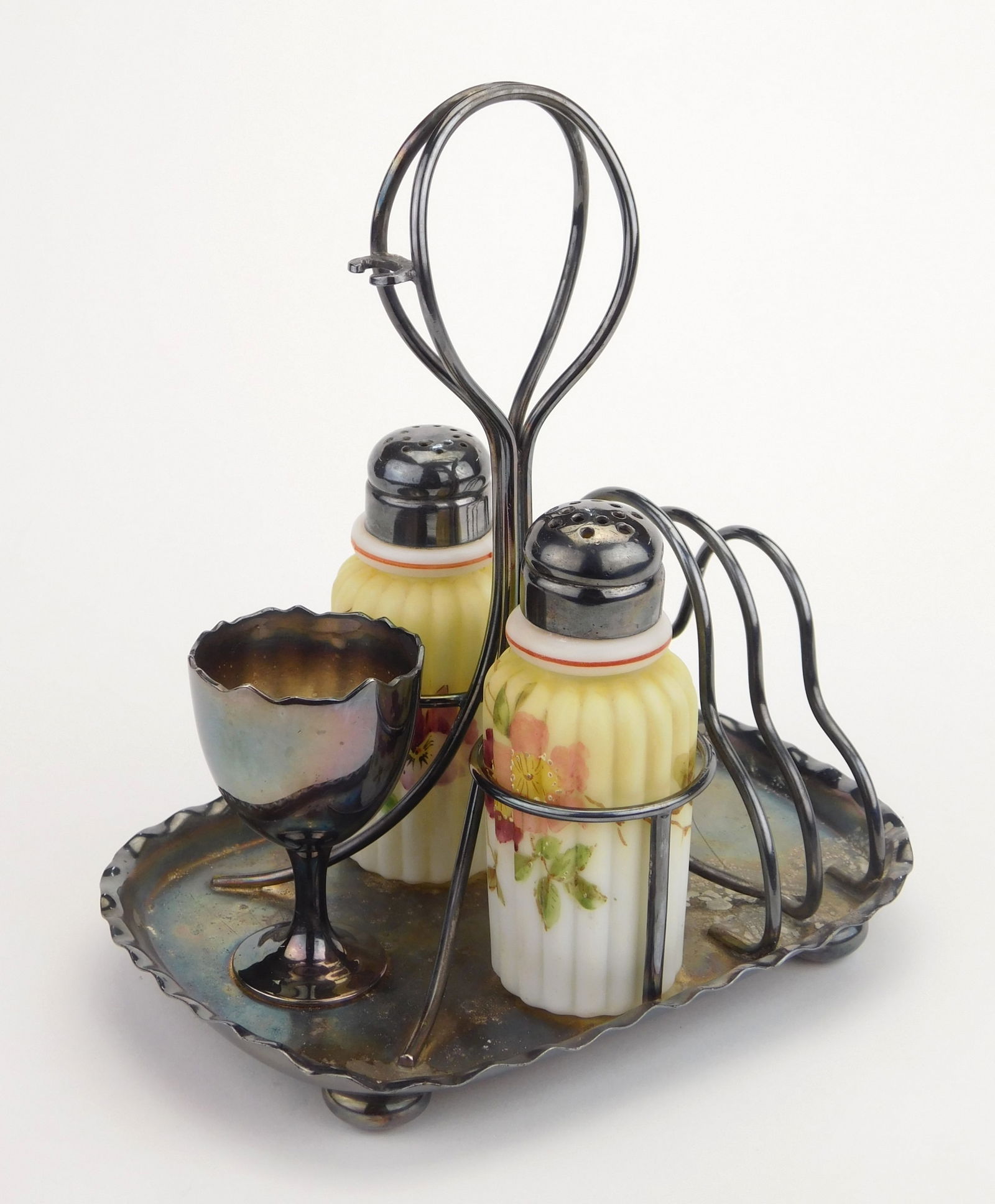 Pairpoint and Mt. Washington condiment set: Pairpoint and Mt. Washington glass condiment set, two Burmese ribbed glass shakers, with a Pairpoint plated caddy with egg cup and toast rack.. Caddy marked on bottom, 6"h