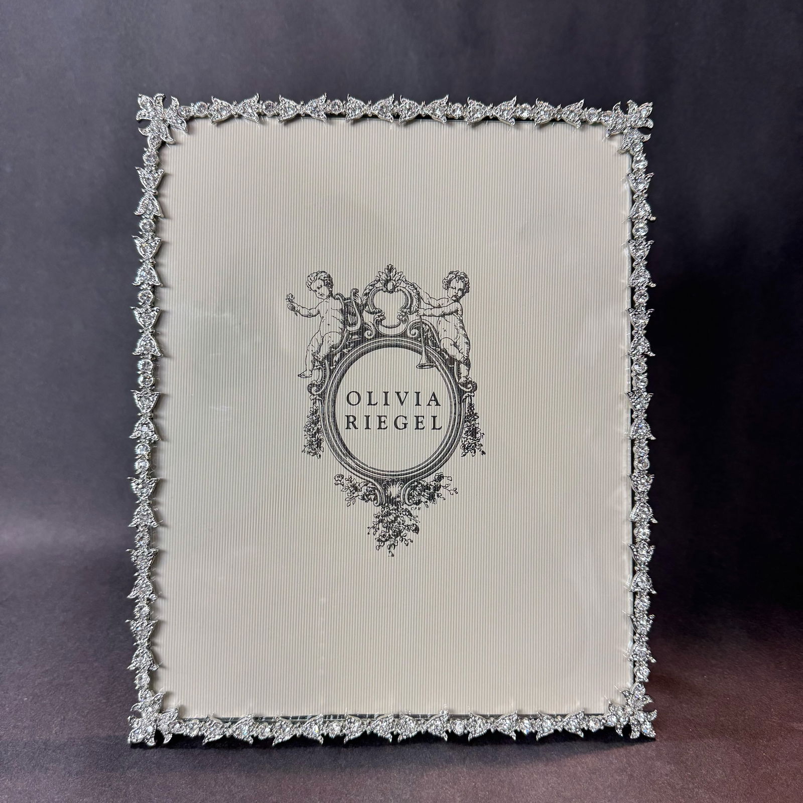 Olivia Riegel Studio 10.75 H x 8.75 W Photo Frame: Artist: Olivia Riegel Studio Title: Luxembourg Frame Medium: Cast pewter in silver finish with hand-set clear Swarovski crystals and gray moire silk backing Size: 10.75 H x 8.75 x 0.5 D Weight: 1.35